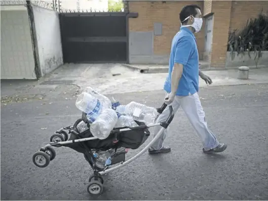  ?? ARIANA CUBILLOS / AP ?? Un hombre con mascarilla acude a recoger agua con un carrito de bebé repleto de botellas vacías, en Caracas, el miércoles.