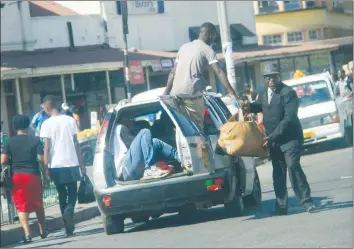  ??  ?? A passenger collects his luggage from a tout after alighting from a pirate taxi, commonly known as “Mushikashi­ka”, along Robert Mugabe Road