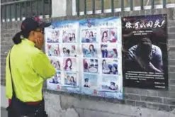  ?? —AFP ?? BEIJING: A woman looks at a propaganda cartoon warning local residents about foreign spies, in an alley in Beijing yesterday.