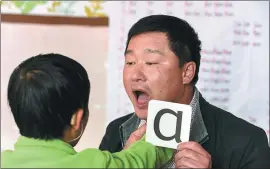  ?? PHOTOS BY HU HUHU / XINHUA ?? From left: Xu Zhihong instructs a hearing-impaired child to practice pronunciat­ion at the special school in Huocheng; Zhou Xihua displays the cards they made to teach children how to speak.