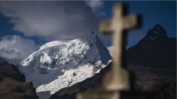  ?? JABIN BOTSFORD/THE WASHINGTON POST ?? An Andes mountain range and a cross headstone are seen from Cementerio Municipal De Huaraz in Huaraz, in the Ancash region of Peru.