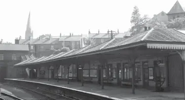  ?? A E Bennett/Transport Treasury ?? The down-side station buildings of Chesterfie­ld (Central) are recorded from an up train as it awaits departure on 7 June 1959. Any passengers looking to go north certainly had plenty of posters to tempt them with products and places to go, and at the distant south end of the station is the stairway leading to the roadside station entrance/exit. Beyond are houses on Brewery Street, and the skyline is pierced by the famous crooked spire of St Mary and All Saints church.