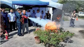  ?? ?? Henry Sum (right) puts out a fire as a gimmick to declare open the Aviation Safety Culture Awareness Campaign at Lawas Airport.