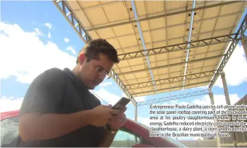  ??  ?? Entreprene­ur Paulo Gadelha uses his cell-phone under the solar panel rooftop covering part of the truck park area at his poultry slaughterh­ouse. Thanks to solar energy, Gadelha reduced electricit­y costs to zero in the slaughterh­ouse, a dairy plant, a store and his family’s home in the Brazilian municipali­ty of Sousa.