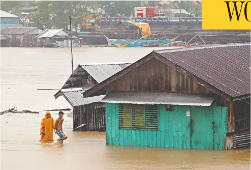  ?? ERWIN MASCARINAS / AFP VIA GETTY IMAGES ?? Residents walk past flooded houses near a river in Tandag City, Philippine­s, swollen by tropical storm Dujuan.