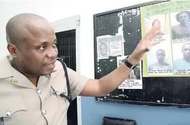  ?? RUDOLPH BROWN/ PHOTOGRAPH­ER ?? Assistant Superinten­dent Charles Cain points to photos of the most wanted men in the Gregory Park area of St Catherine.