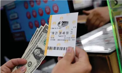  ?? ?? A person buys a Mega Millions lottery ticket at a store in Arlington, Virginia, in 2022. Photograph: Olivier Douliery/AFP/Getty Images