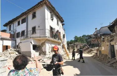  ?? Alberto Pizzoli / AFP / Getty Images ?? A firefighte­r helps a resident of Rio, Italy, recover belongings from a house damaged in the 6.2 earthquake.