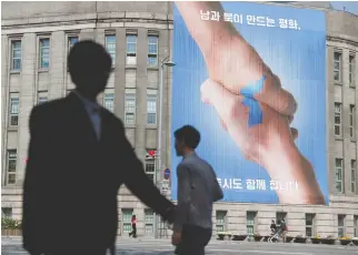  ??  ?? PEOPLE WALK past a large banner adorning the exterior of City Hall ahead of the upcoming summit between North and South Korea in Seoul, South Korea on April 25.