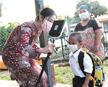  ??  ?? A teacher of Sekolah Rendah Buit Hill in Kota Kinabalu helping a year one pupil to check his temperatur­e when he arrived at school yesterday. A total of 824 primary schools in Sabah opened for lessons yesterday by following the standard operating procedures strictly.-Bernama photo