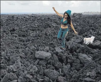  ?? Marco Garcia The Associated Press ?? Tisha Montoya and her dog Bebe cut through the lava field that covered much of her property and destroyed her home near Pahoa, Hawaii, when Kilauea erupted in 2018.