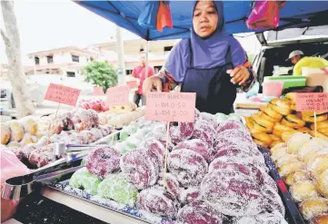  ??  ?? Nor Nafishah arranging doughnuts in fanciful colours and varieties at her stall at Chandan Puteri in Kuala Kangsar. — Bernama photo