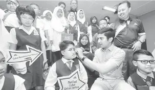  ?? — Gambar Bernama ?? RAMAH MESRA: Syed Saddiq (duduk, dua kanan) memakaikan cermin pada pada murid Muhamad Adam Hariz Syarizam 10 pada Majlis Penyerahan Program Tanggungja­wab Sosial Lembaga Hasil Dalam Negeri (LHDN) di Sekolah Kebangsaan Parit Nombor Lima dekat Muar,...