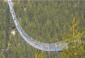  ?? PETR DAVID JOSEK/AP ?? Pedestrian­s cross a suspension bridge shortly after its official opening Friday at a mountain resort in Dolni Morava, Czech Republic. The bridge, which is the longest structure of its kind in the world at more than 2,300 feet long and strung at an altitude more than 3,600 feet above sea level, affords those who traverse the span views of a valley 311 feet below.