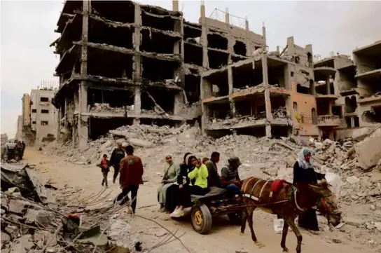  ?? AFP VIA GETTY IMAGES ?? A Palestinia­n family rode next to damaged buildings in Khan Younis Monday after Israel pulled out its ground forces.