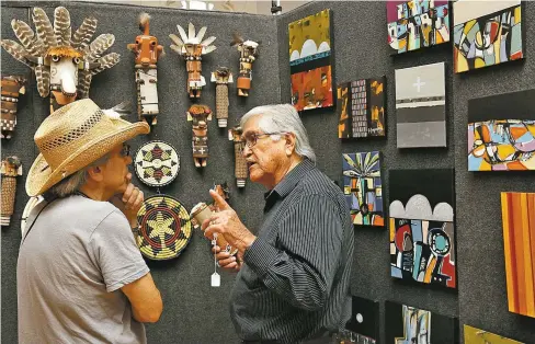  ??  ?? ABOVE: Manfred Susunkewa, right, of the Hopi Tribe chats with a visitor about the kachinas in his booth, which also features coil baskets made by his wife, Norma, and paintings by his daughter, Sheryl, on Saturday during the Free Indian Market Show at the Scottish Rite Center.