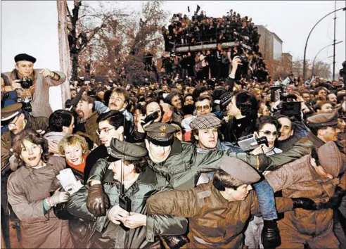  ?? PATRICK HERTZOG/GETTY-AFP ?? East and West German police contain the crowd of East Berliners flowing through the recent opening made in the Berlin wall at Potsdamer Square on Nov. 12, 1989.