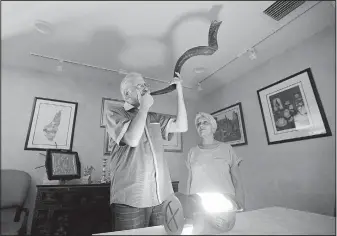  ?? The Associated Press/ALAN DIAZ ?? Michael Andron blows the shofar as he prepares for Rosh Hashana, and his wife, Lillian, watches as they use a battery-powered lantern to illuminate the room at their home in Miami. As of Tuesday, the Androns had been without power for nine days due to...