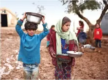  ?? Walking in the mud, Syrian children carry pots of food at a refugee camp near Shamarin village in the northern Aleppo province, on Sunday. ??