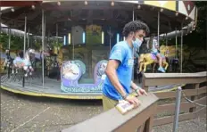  ?? Lucy Schaly/Post-Gazette ?? Staff member Justin Barnham, 17, of Hazelwood, closes the gate of the Merry Go Round ride after it is partially filled with riders at the Pittsburgh Zoo & PPG Aquarium, which reopened its doors to the public on Friday.