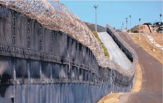  ?? GARY CORONADO / LOS ANGELES TIMES/TNS ?? A U.S. Border Patrol agent, San Diego Sector, patrols along the secondary fence along the U.S.-Mexico border with Tijuana in San Diego, Calif., on July 27, 2017. Video surveillan­ce camera, left, and stadium lighting can be seen in the background.