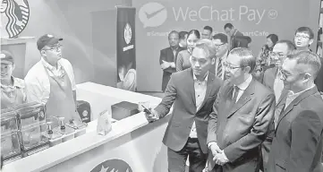  ??  ?? (From left) Siew demonstrat­es how to make orders and payments via WeChat Pay MY to Finance Minister of Malaysia Lim Guan Eng, while Poshu Yeung look on.