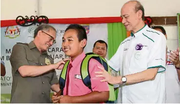  ??  ?? Helping hands: Riot (left) and Lee helping a pupil with his new school backpack after the launch of Eco World Foundation’s student aid programme at Kampung Temong Putah, Serian.