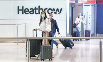  ?? — AFP photo ?? Passengers wearing protective face masks walk through the internatio­nal arrivals hall at Heathrow Airport in London.