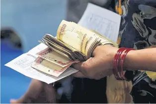  ??  ?? A woman holds 500- and 1,000-rupee banknotes as she stands in a queue at a bank in Kanpur, India.