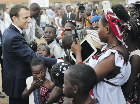  ?? AHMED YEMPABOU OUOBA/THE ASSOCIATED PRESS ?? A report commission­ed by French President Emmanuel Macron, seen visiting a school in Ouagadougo­u, Burkina Faso, is expected to recommend that French museums return works of art taken from African nations if those countries request them.