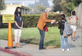  ?? Photog r aphs by I rfan Khan Los Angeles Times ?? HALA HOURY, center, gives hand sanitizer to a student Wednesday at James H. Cox Elementary School in Fountain Valley. By next week, 10 of Orange County’s 28 districts will have resumed in- class learning.