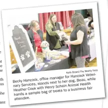  ?? Keith Bryant/The Weekly Vista ?? Becky Hancock, office manager for Hancock Veterinary Services, stands next to her dog, Beau, while Heather Cook with Henry Schein Animal Health hands a sample bag of treats to a business fair attendee.