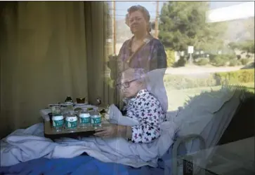  ?? Francine Orr Los Angeles Times ?? MARJORIE LEACH eats lunch at Mountain View Convalesce­nt Hospital in Sylmar. After being quarantine­d with COVID-19, she went home in December. Ref lected in the window is one of her daughters, Kathleen Hill.