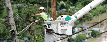  ??  ?? In this May 16 file photo, a worker from the Cobra Energy Company, contracted by the Army Corps of Engineers, installs power lines in the Barrio Martorel area of Yabucoa, a town where many residents continue without power in Puerto Rico. AP PhoTo/CArloS gIuSTI