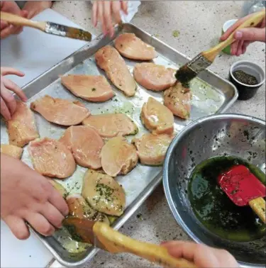  ?? SUBMITTED ?? Young hands of those enrolled in a Paganini school cooking camp swab chicken breasts with oil and herbs prior to sauteing them.