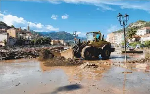  ?? FEDERICO SCOPPA AFP VIA GETTY IMAGES ?? A bulldozer clears the mud near a collapsed walkway by the Roya River in Ventimigli­a, Italy, on Saturday after heavy rain caused flooding that have submerged the city with water and mud.