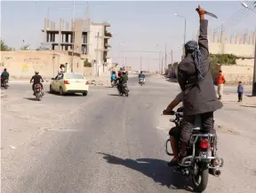  ?? (Reuters) ?? A MAN holds up a knife as he rides through the streets of Tabqa after Islamic State took over the Iraqi air base, in 2014.