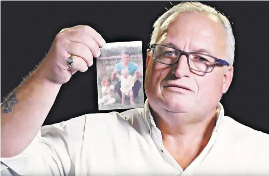  ??  ?? Alan Burgess holds a photograph of himself with his children in 1986, just prior to his diagnosis with HIV and Hepatitis C