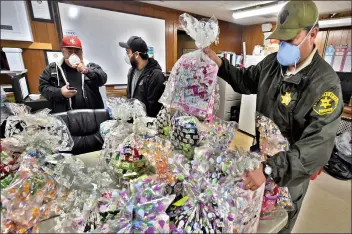  ?? Dan Watson/The Signal ?? (Above) Santa Clarita Valley Sheriff’s Deputy Brian Rooney, right; Jaime Briano, left; and Darwin Lorenzo, of the of Los Angeles County Department of Parks and Recreation, sort through the 50 Easter baskets prepared for Youth Activity League children in Val Verde on Thursday. (Top right) Briano and Natalie Ramirez, of Santa Clarita Valley Sheriff’s Foundation’s Youth Activity League, deliver Easter baskets Thursday. (Right) Lorenzo and Ramirez carry some of the baskets to a van for delivery.