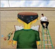  ?? TANIA BARRICKLO — DAILY FREEMAN FILE ?? Kingston, N.Y., artist Eugene Seitz sits on a ladder in front of his a he painted on the side of The People’s Place on St. James St. in the city during the 2016 O+ Festival.