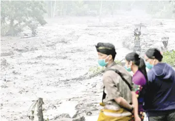  ??  ?? Villagers watch a river overflowin­g with water mixed with volcanic ash during the eruption of Mount Agung in Karangasem, Bali. — Reuters photo