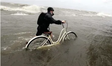  ?? Associated Press ?? ■ Tyler Holland guides his bike through water Saturday as winds from Tropical Storm Barry push Lake Pontchartr­ain over the seawall in Mandeville, La.