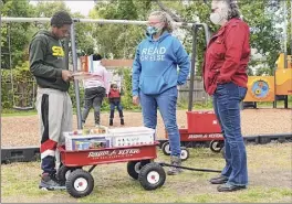  ??  ?? Seven Chandler of Albany picks out books from a RED Bookshelf wagon for his son Treasjour, 4, who is on the swing, at Black Lives Matter Park. Rachel Eveleth, second from right, and Mary Beth Fowler, who founded the program, were pulling the wagon around the area.