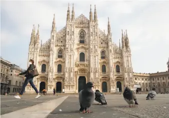  ?? Antonio Calanni / Associated Press ?? A woman walks across the normally bustling plaza outside the Milan Cathedral. The Lombardy region is among four in Italy where new coronaviru­s restrictio­ns went into effect on Friday.