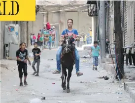  ?? THAER MOHAMMED / AFP / GETTY IMAGES ?? A boy rides a horse as children play in the street in the Syrian city of Aleppo. A fragile ceasefire appeared to be holding Tuesday, according to residents and activists, raising hope that humanitari­an aid would soon be delivered to besieged areas.