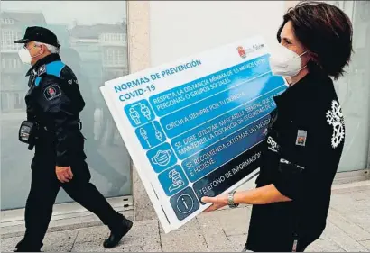  ?? ELISEO TRIGO / EFE ?? Una mujer coloca un cartel informativ­o sobre la Covid-19 en una calle de Viveiro, en la comarca de A Mariña