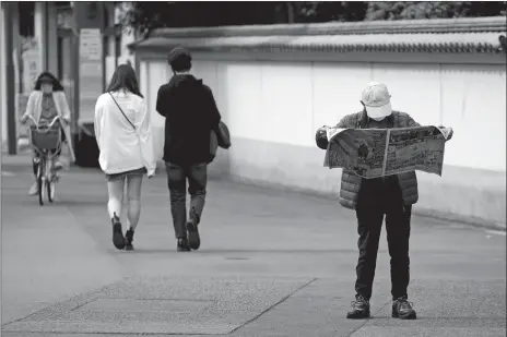  ?? EUGENE HOSHIKO/AP PHOTO ?? A man wearing a protective mask to help curb the spread of the coronaviru­s reads a newspaper near Asakusa district Thursday in Tokyo.