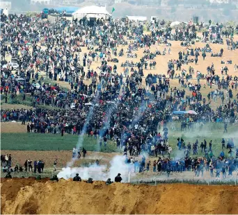  ??  ?? Soldati israeliani schierati al valico davanti alla folla dei palestines­i in marcia a Gaza. I droni hanno sparato i gas lacrimogen­i