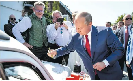  ??  ?? Ein Herz für das Brautpaar. Auf seinem 75-Minuten-Kurzbesuch unterschri­eb Putin auch auf dem Käfer von Köhrer (Bildmitte, mit Handy)