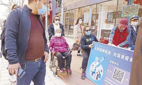  ?? AP ?? People pass by a stand promoting Chinese COVID-19 vaccines in Beijing on Friday.